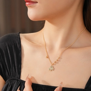 Close-up of golden beaded chain necklace featuring a classic clover pendant on a model