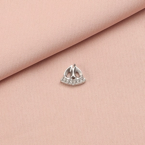 Macro detail of silver stainless steel crown pendant accessory on pink fabric background