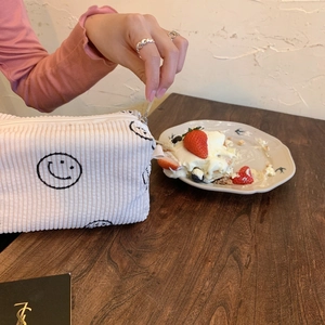 Detail of off-white corduroy cosmetic bag with embroidered smiley face on wooden table