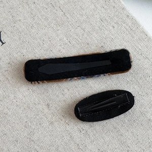 Close-up of hair clip back view with black metal duckbill clips and felt lining on beige fabric
