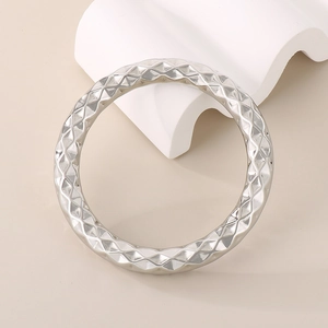 Minimalist silver stainless steel bangle with geometric diamond patterns on a white pedestal