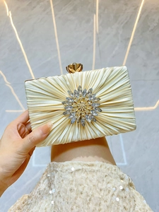 Detail einer champagnerfarbenen Seiden-Abendtasche mit großer Strassblume und Falten