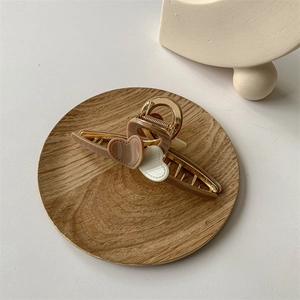 Close-up of a beige heart hair claw clip on a wooden tray with golden metal spring