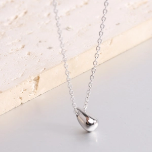 Minimalist polished silver teardrop pendant necklace on a natural stone background