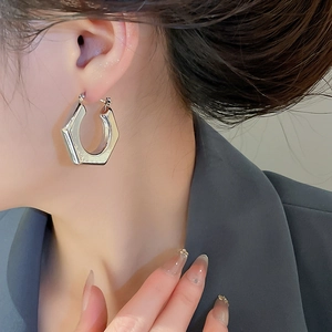 Close-up of polished silver hexagonal geometric hoop earrings worn by a model