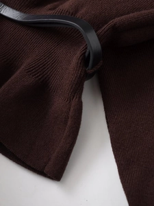 Nahaufnahme der Stricktextur mit schwarzem Ledergürtel-Detail auf brauner Strickware