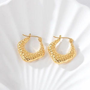 Gros plan de boucles d'oreilles dorées en U avec texture martelée sur plateau