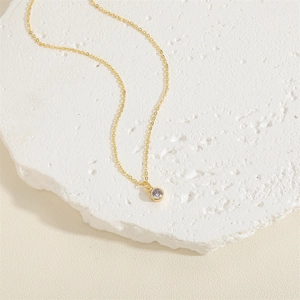 Minimalistische 14K vergoldete Halskette mit lila Zirkonia Anhänger auf weißem Steinhintergrund