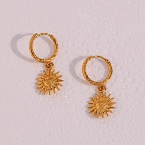 Macro detail of golden sun-face charms on vintage stainless steel hoop earrings