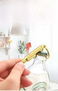 Macro shot of a gold bullet-shaped bottle opener keychain opening a glass bottle