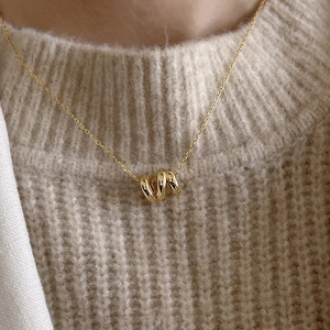 Close-up of gold ripple pendant necklace worn on a beige knit sweater for minimalist style