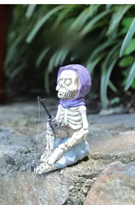 Macro detail of skeleton figurine with purple bandana fishing on rock for garden decor