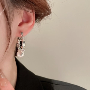 Close-up of geometric silver metal earrings with white round pearls on a female model
