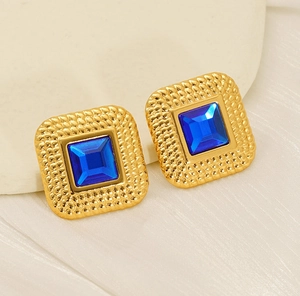 Macro shot of gold square stud earrings with blue zircon and vintage hammered texture