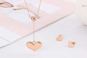 Rose gold heart pendant necklace and earrings set on a white surface with magazine