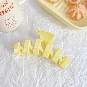 Detail of light yellow matte hair claw clip on soft white crinkle paper background