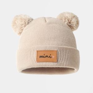 Detail of baby winter knit hat featuring cute pom-pom ears and a mini leather patch