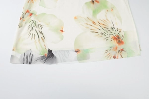 Detail shot of sheer white mesh fabric featuring elegant green and black floral patterns
