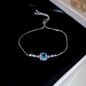 Detail of silver bracelet with square blue gemstone and crystal accents on black background
