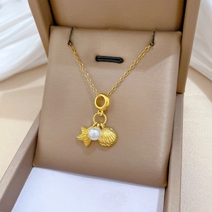Detail of gold necklace with star, shell, and pearl charms on white silk fabric