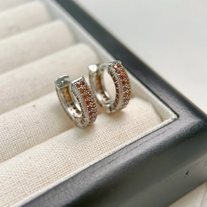 Detailed macro view of silver hoop earrings with triple-row micro-paved orange gemstones