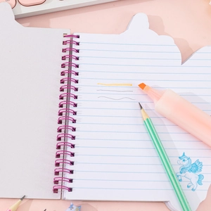 Plush rainbow unicorn notebook with purple spiral binding on a creative desk setting