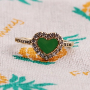 Dettaglio dell'anello dorato con gemma verde a cuore e pavé di zirconi scintillanti