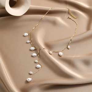 Detail of Y-shaped golden necklace featuring baroque pearls on champagne satin fabric