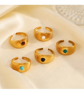 Top view of five adjustable gold stone rings with radial stripes on soft silk fabric