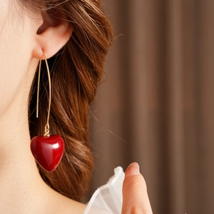 Macro detail of model wearing vintage red heart pendant earrings with elegant gold hooks