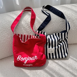Close-up of red and blue striped canvas tote bags with Bonjour print on soft sofa