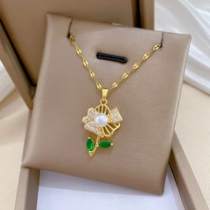 Detail showing a gold flower pendant with green stones and a pearl in a gift box