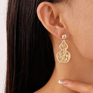 Macro view of gold flower hollow gourd earrings featuring zircons on a female model