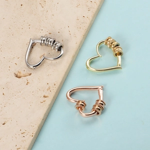 Close-up of heart-shaped spring earrings in silver, gold, and rose gold on a stone base