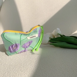 Macro detail of tulip embroidery and yellow zipper on a green fabric cosmetic bag