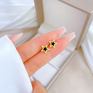 Minimalist titanium steel star earrings with gold border and black inlay held in fingers
