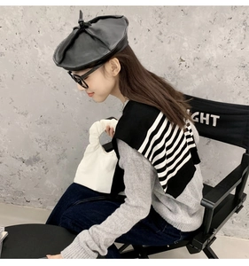 Detail of a chic black and white striped knit shawl worn with a black PU leather beret hat