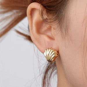 Close-up of a model wearing a golden shell-shaped earring with polished fan texture