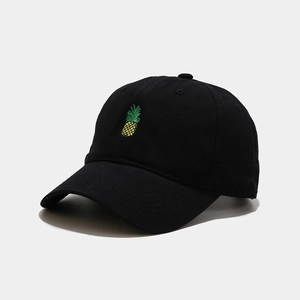 Close-up of golden pineapple embroidery on black cotton twill baseball cap with curved brim