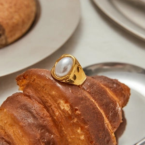 Close-up of a gold stainless steel pearl ring placed on a croissant for a luxury aesthetic