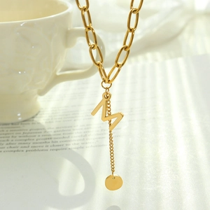 Golden chunky chain necklace with M letter pendant and round tag on vintage background