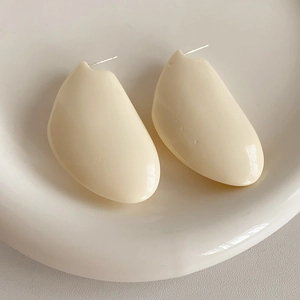 Détail de boucles d'oreilles irrégulières en résine blanc cassé sur une assiette blanche
