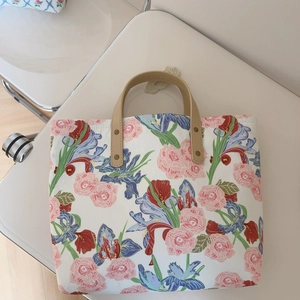 Detailed shot of canvas tote bag with floral patterns and leather handle on white chair