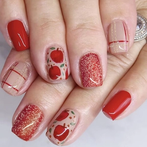 Detailed close-up of glossy red and beige press-on nails with apple and plaid patterns