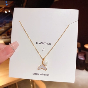 Detailed view of elegant fishtail pendant with white pearl on gold chain necklace