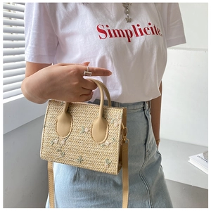 Detail of straw woven bag featuring delicate pink flower embroidery and leather handle