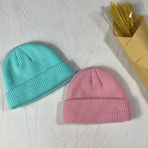 Flat lay detail of mint green and pink knit beanies on white texture with wheat