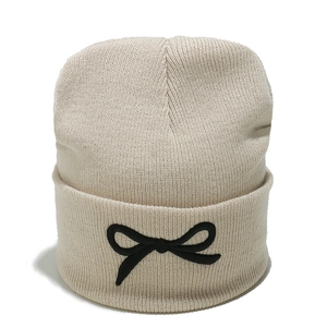 Détail d'un bonnet en tricot beige orné d'un nœud noir brodé sur le bord plié classique