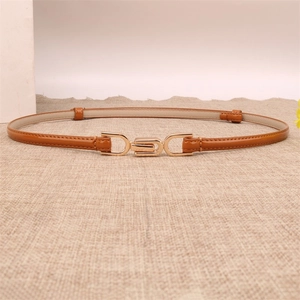 Detail of slim caramel leather belt with gold interlocking metal buckle on textured fabric