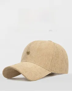 Close-up of khaki herringbone fabric baseball cap with small gold heart metal logo detail